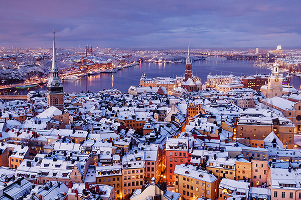 Verschneite Altstadt an der Ostsee mit Kirchtürmen, beleuchteten Häusern und Hafenbecken.