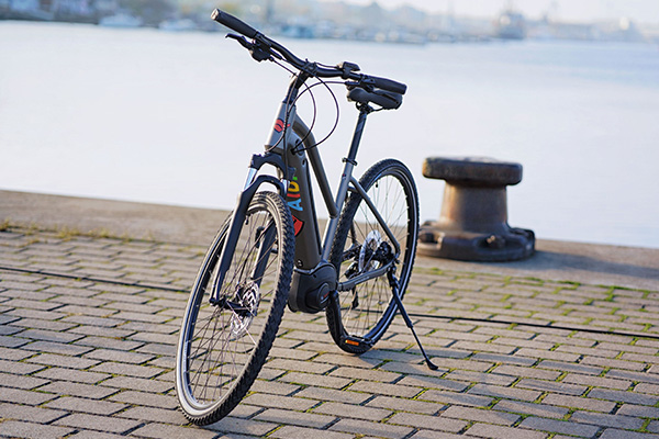 Schwarzes E-Bike auf einer gepflasterten Uferpromenade vor dem Wasser.